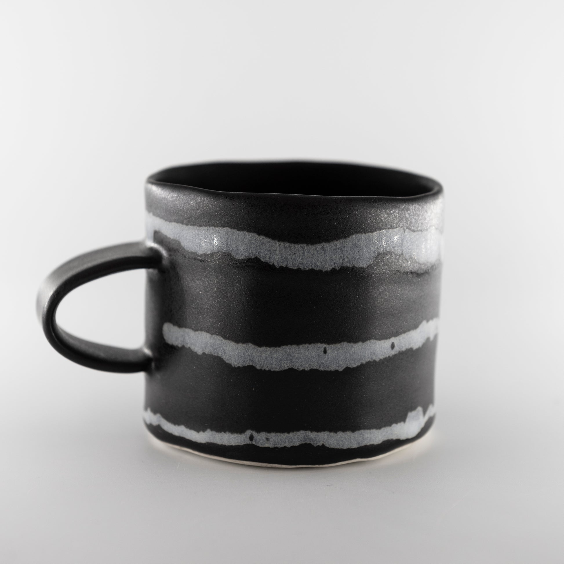 Black mug with grey irregular sized horizontal stripes around it.
