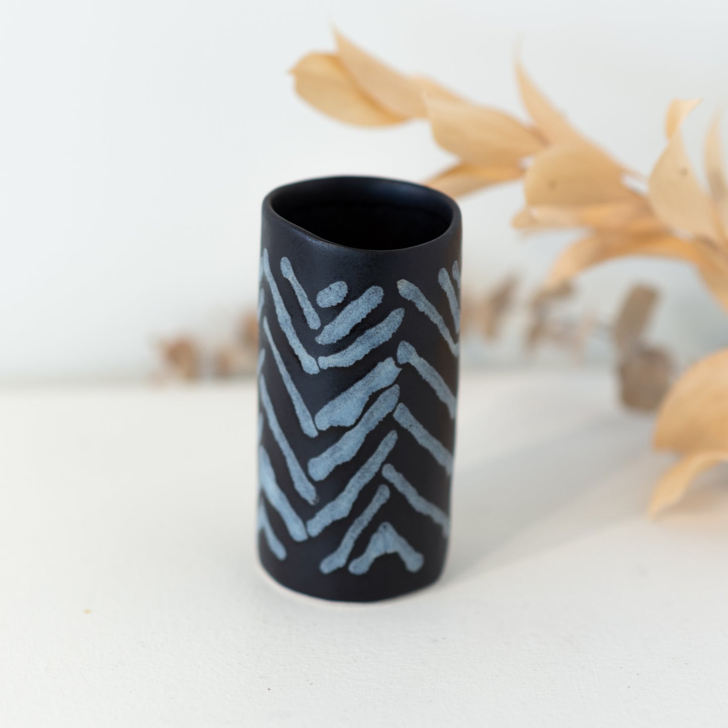 Black vase with white/grey chevron in front of a dried plant.