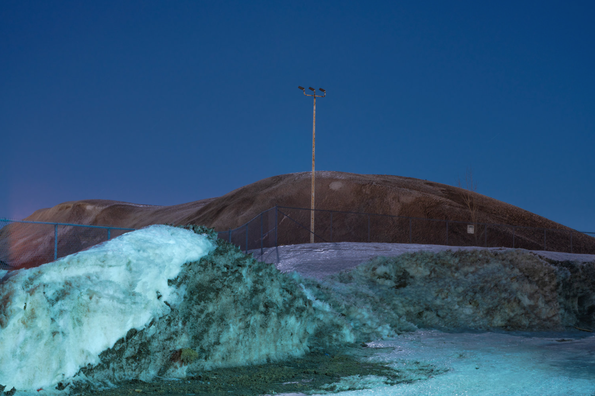 Thawed and dirt covered snow piles during the blue hour.