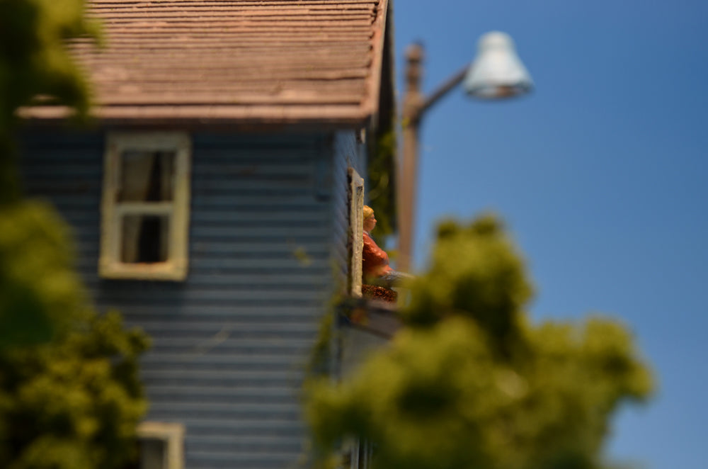 Photograph of a miniature diorama, featuring a sideview of a house with a pregnant woman standing on a balcony.